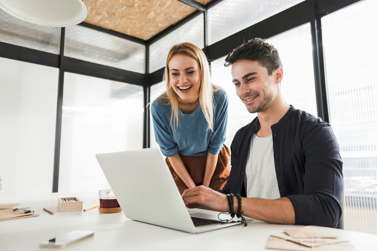 Lächelndes Paar arbeitet gemeinsam am Laptop in einem hellen Büro